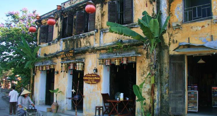 Weathered yellow-plaster shophouse in Hoi An Old Town adorned with red lanterns and banana plants.