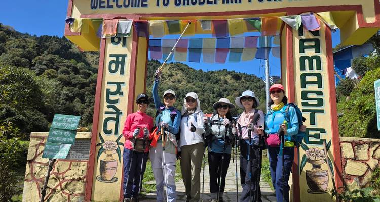 Six trekkeurs se tiennent sous une porte d'entrée colorée ornée de drapeaux de prière accueillant les visiteurs à Ghandruk.