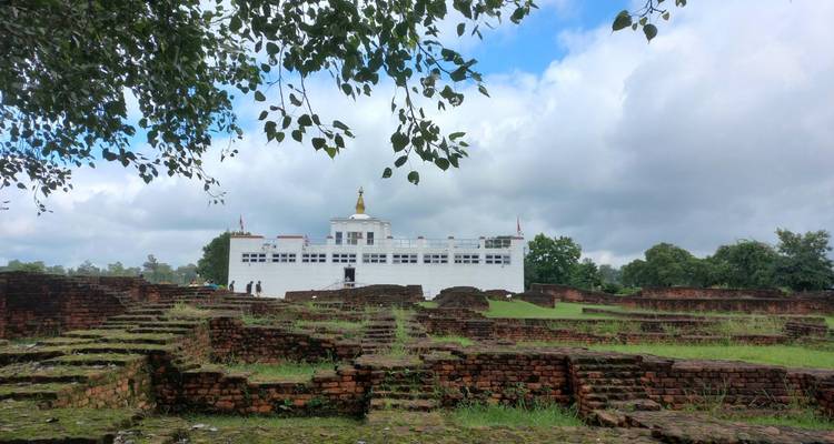 Le temple blanc Maya Devi s'élève derrière des ruines de briques anciennes et des pelouses vertes sous un ciel partiellement nuageux à Lumbini.
