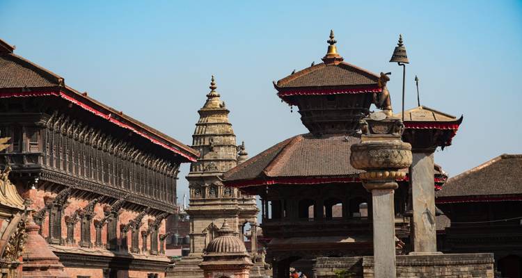 Les pagodes ornées et les façades en bois sculpté des palais dominent la ligne d'horizon de la place Bhaktapur Durbar sur un ciel bleu dégagé.