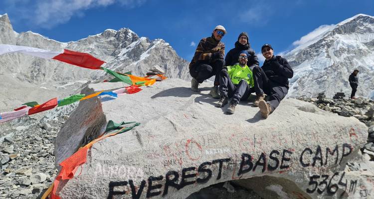 Groep wandelaars die poseren op de beroemde Everest Base Camp steen bedekt met gebedsvlaggen.