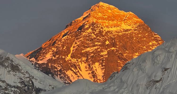 Mount Everest verlicht in vurig oranje licht tijdens zonsopgang tegen een donkere lucht.