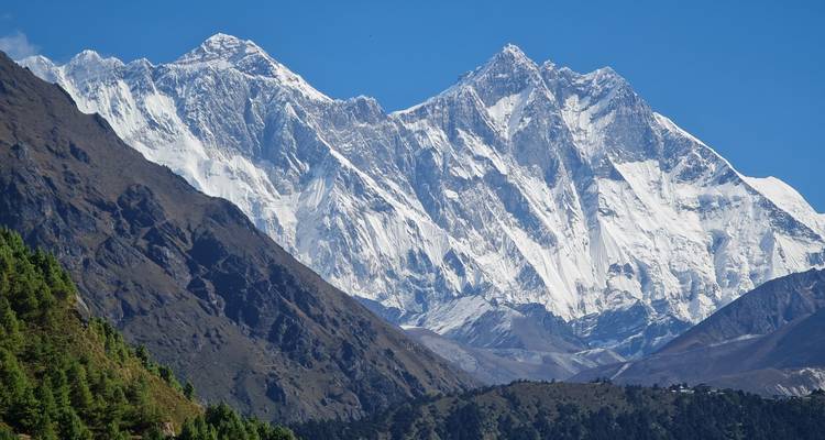 Helder daglicht uitzicht op het Everest-massief met scherpe, met sneeuw bedekte bergtoppen die boven groene voethellingen uitsteken.