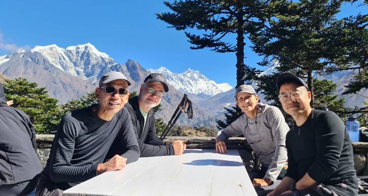 Trekkingstokers die zich ontspannen aan een buitentafel met panoramische Himalaya-pieken op de achtergrond.