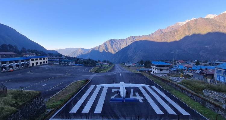 Uitzicht over de steile landingsbaan van Lukla airport met een klein vliegtuig dat klaar staat om op te stijgen tussen bergachtig landschap.