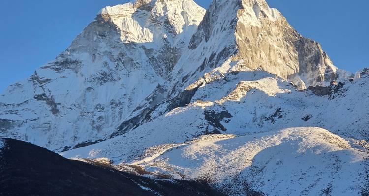 Close-up van een ruige, sneeuwbedekte Himalayatop ondergedompeld in warm avondlicht.