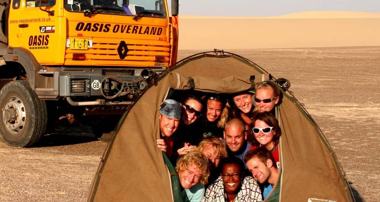 Groupe de personnes à l'intérieur d'une tente avec un camion tout-terrain en arrière-plan.