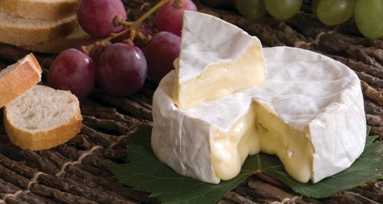 Cheese wheel with sliced wedge, accompanied by grapes and bread