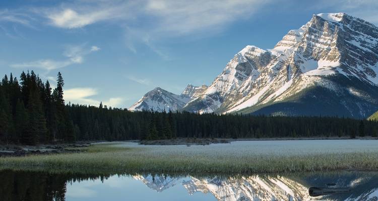 Schneebedeckter Berg neben einem See mit Spiegelung.