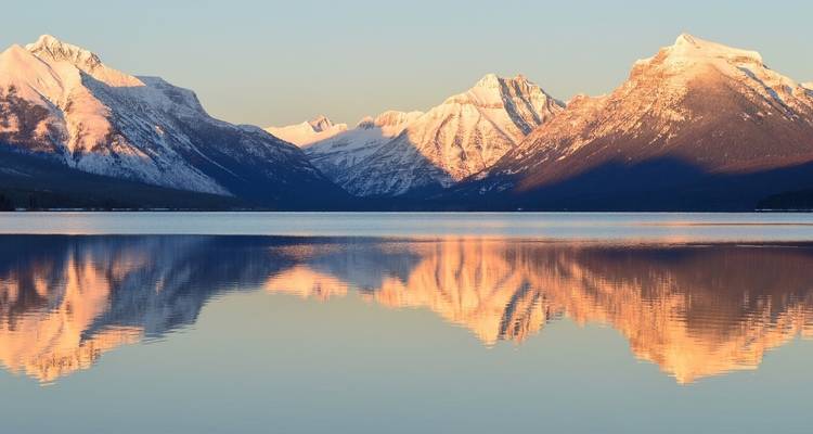 Sonnenaufgang oder Sonnenuntergang über einem ruhigen See mit Bergen im Hintergrund.