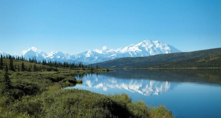 Un lago sereno que refleja montañas cubiertas de nieve y un cielo azul despejado.