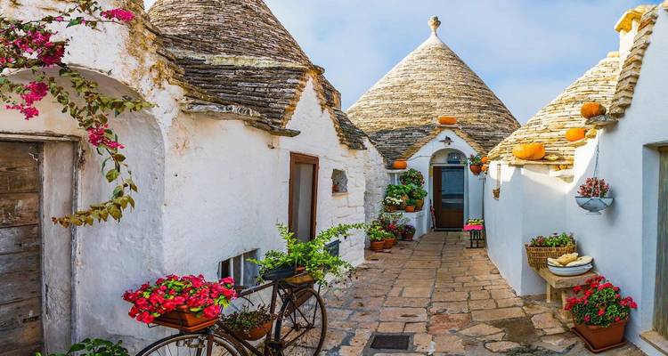 Pintorescas casas trulli encaladas con techos cónicos de piedra y macetas de flores vibrantes en Alberobello.