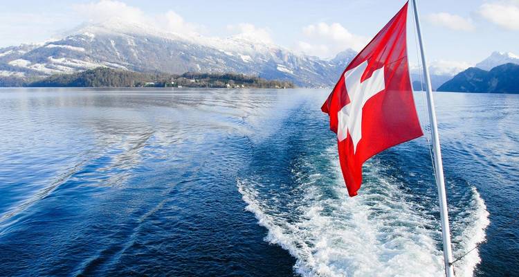 Drapeau suisse flottant depuis un bateau sur un lac avec des montagnes en arrière-plan.