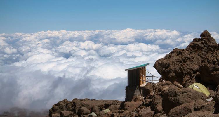 Een rustieke schuilplaats gebouwd tegen een rotsachtige berg achtergrond boven de wolken.