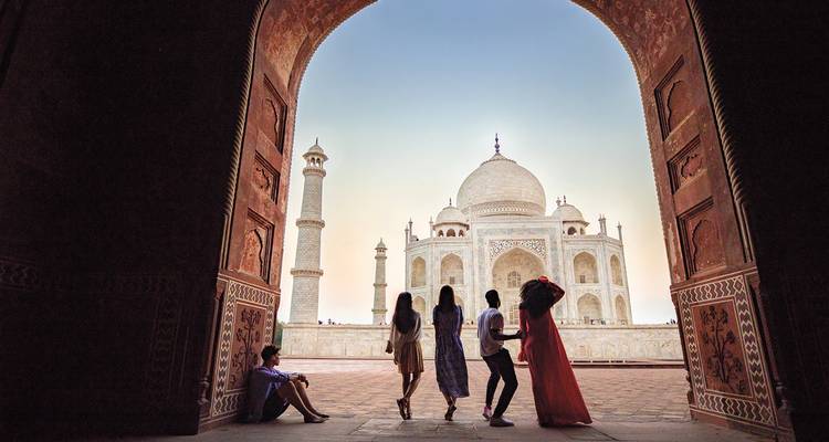 Silhouettierte Besucher rahmen das Taj Mahal durch einen großen Sandsteinbogen im Morgengrauen ein