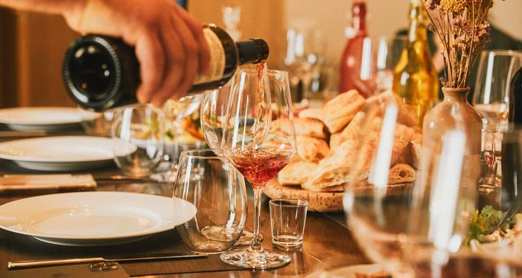 Se vierte vino en copas elegantes sobre una mesa rústica servida con panes y aperitivos.