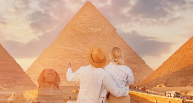 Una pareja se abraza mientras observan las Grandes Pirámides y la Esfinge bajo un cielo cálido y resplandeciente.