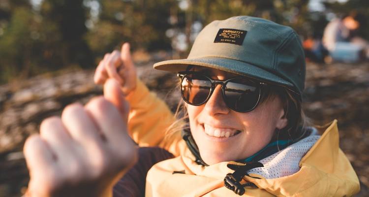 Gros plan d'une personne assise avec des arbres en arrière-plan portant une casquette et des lunettes de soleil.