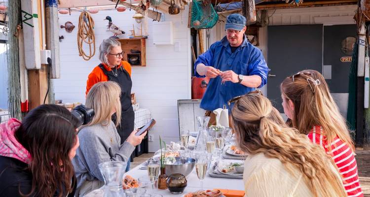 Groep mensen die dineert terwijl een chef eten presenteert in een rustieke omgeving.