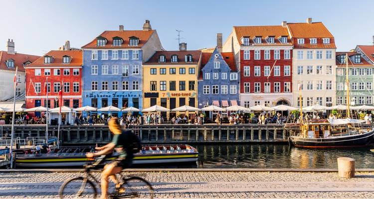 Bunte Reihenhäuser entlang Kopenhagens Nyhavn-Kanal mit einem verschwommenen Radfahrer im Vordergrund.