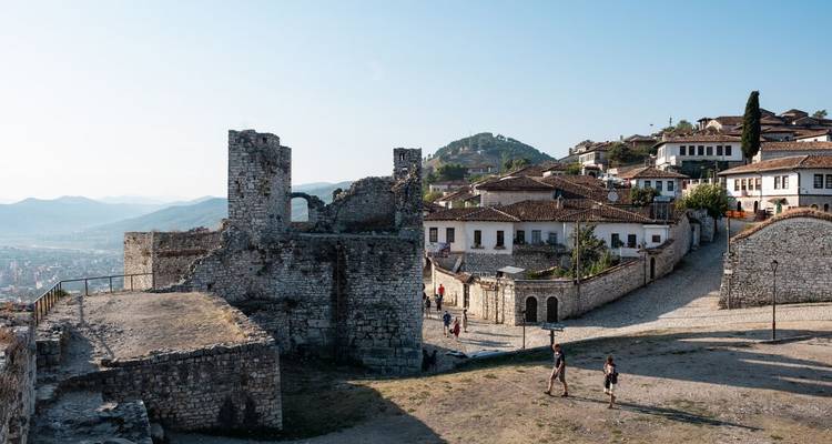 Ruines d'une forteresse historique avec des bâtiments environnants aux toits de tuiles.
