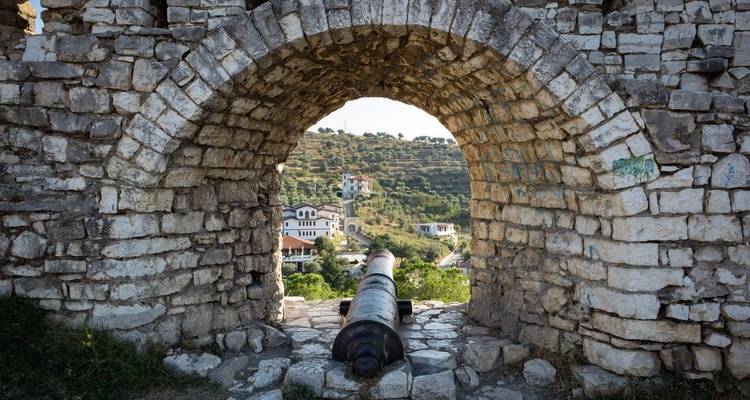 Vue à travers une arche de pierre avec un canon, donnant sur la campagne.