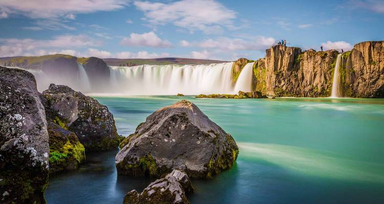 Majestätischer Wasserfall, der in einen türkisfarbenen Fluss mit felsiger Umgebung stürzt.