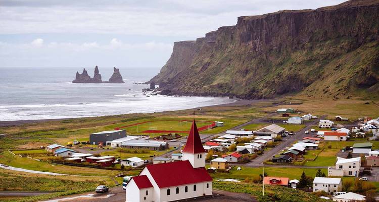 Ein malerisches Dorf mit einer rotgedeckten Kirche und dramatischen Klippen mit Blick auf den Ozean.