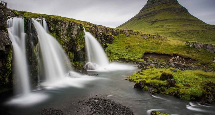 Wasserfall mit üppigem Grün und einem spitzen Berg im Hintergrund.