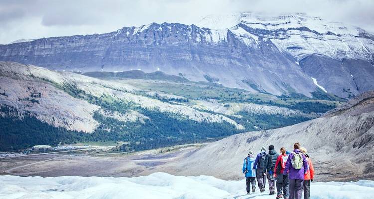 Des gens marchant sur un glacier avec une vue sur des montagnes spectaculaires.