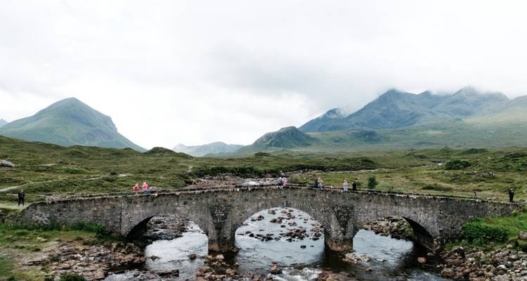 Puente de piedra sobre un río con personas explorando la zona.