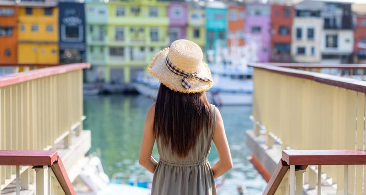 Femme avec un chapeau regardant des bâtiments colorés au bord de l'eau.