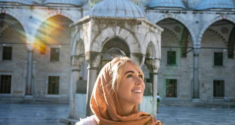 Jeune femme souriante devant un bâtiment historique avec des dômes.