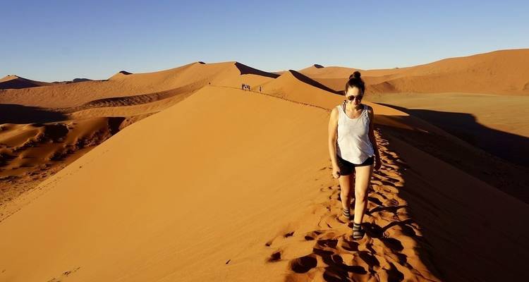 Mujer caminando por una duna de arena en el desierto.