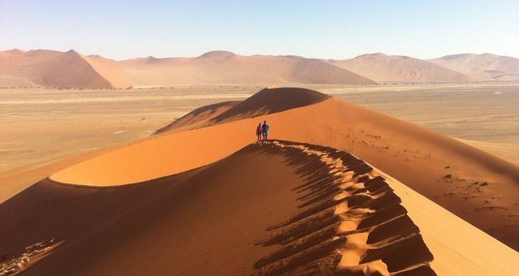 Dos personas caminando por la cresta de dunas rojas del desierto.