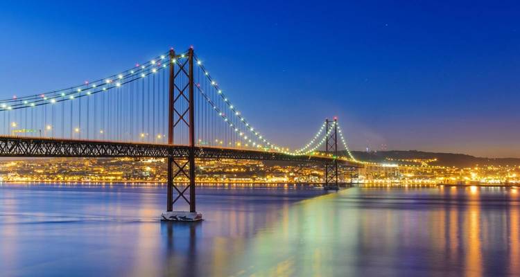 Un puente colgante bellamente iluminado sobre el agua al atardecer.