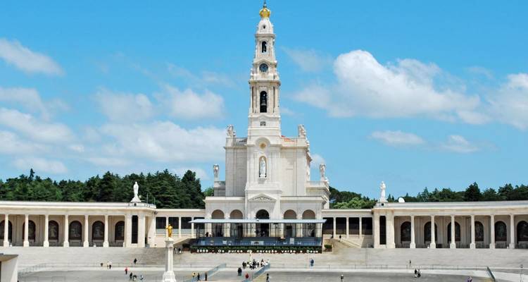 Una gran basílica con estatuas en una amplia plaza bajo un cielo azul.