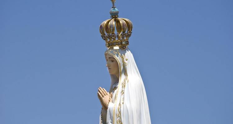 Una estatua de una mujer coronada en oración bajo un cielo azul despejado.