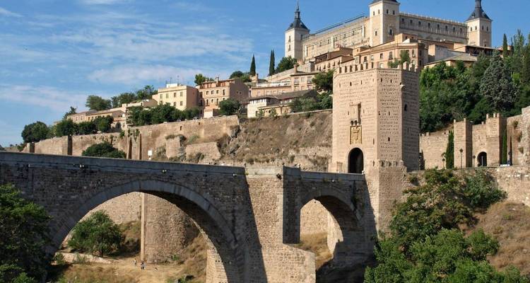 Un majestuoso puente de piedra que atraviesa un río con un paisaje urbano histórico.