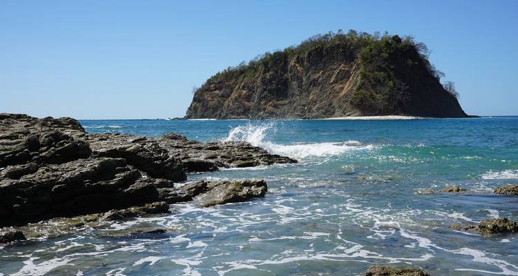 Côte rocheuse avec des vagues océaniques et une île au loin.