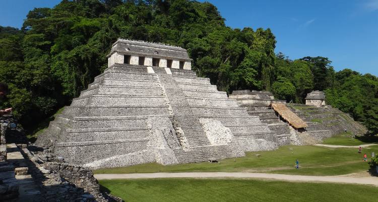 Temple pyramid at Palenque surrounded by dense jungle under a clear blue sky