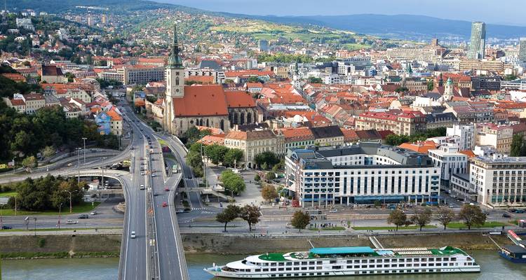 Panoramablick über Bratislavas rotgedeckte Altstadt, Kathedrale und die Donau mit einem weißen Kreuzfahrtschiff