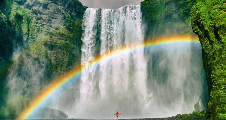Grande cascade avec un arc-en-ciel et une silhouette solitaire devant.