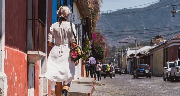 Woman in white dress walking along a colorful colonial street in Antigua with bustling activity