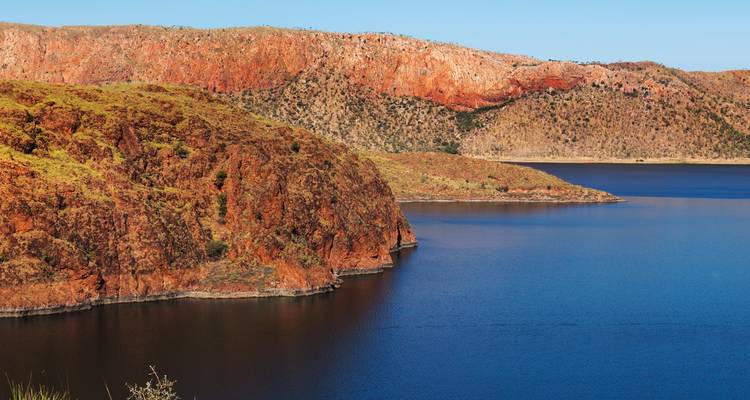 Lac entouré de formations rocheuses rouges sous un ciel bleu.