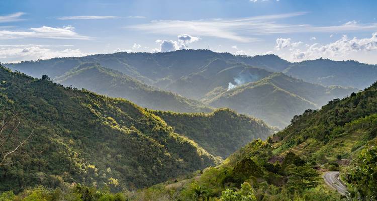 Les crêtes ensoleillées des montagnes verdoyantes luxuriantes du Sabah avec une route sinueuse en contrebas.