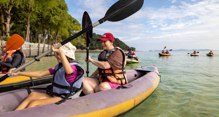 Des personnes naviguant en kayaks gonflables sur une mer peu profonde et cristalline près d'une côte tropicale.