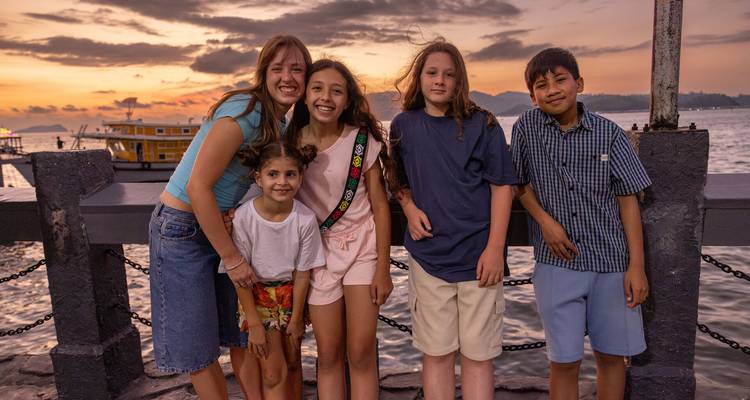 Groupe d'enfants souriants debout sur un quai au coucher du soleil avec la mer en arrière-plan.
