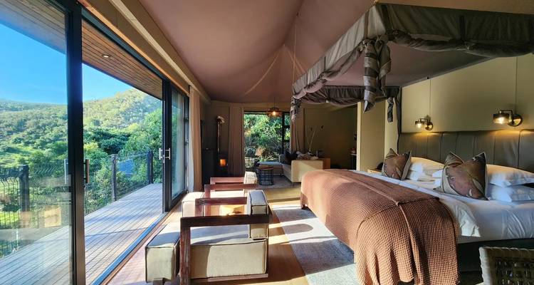 Spacious luxury tented suite with canopy bed opens onto a deck overlooking green hills.