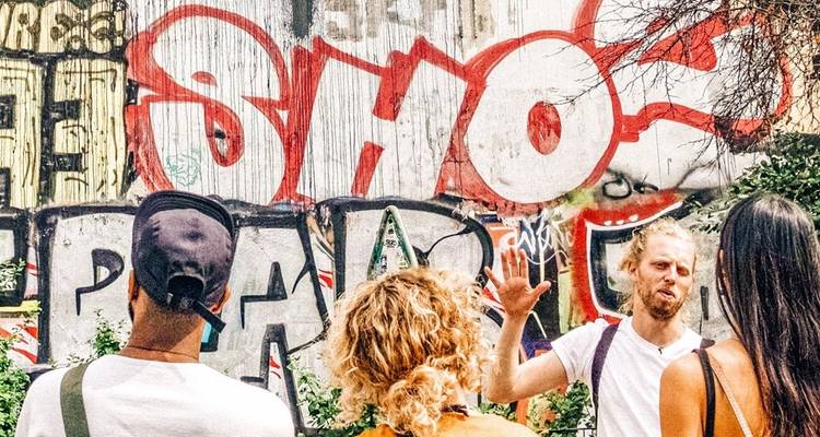 Petit groupe de touristes écoute un guide devant un mur vibrant couvert de graffitis